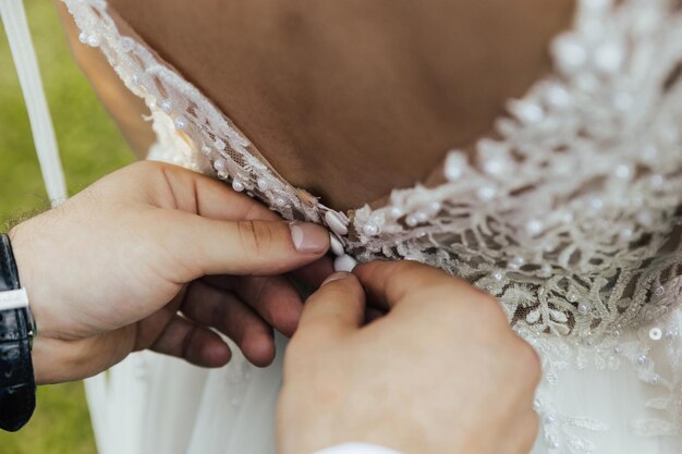 Foto le mani dello sposo allacciano i bottoni sul vestito della sposa