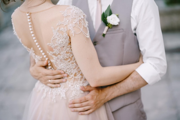 Hands of groom on the waist of bride in an embroidered lace dress closeup