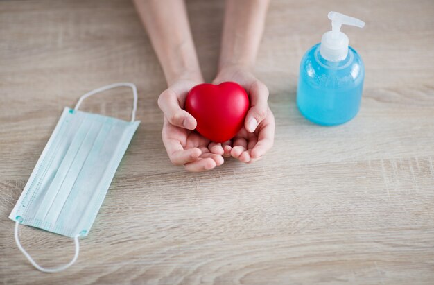 in the hands of a guy a red heart, a hand disinfector and a protective mask