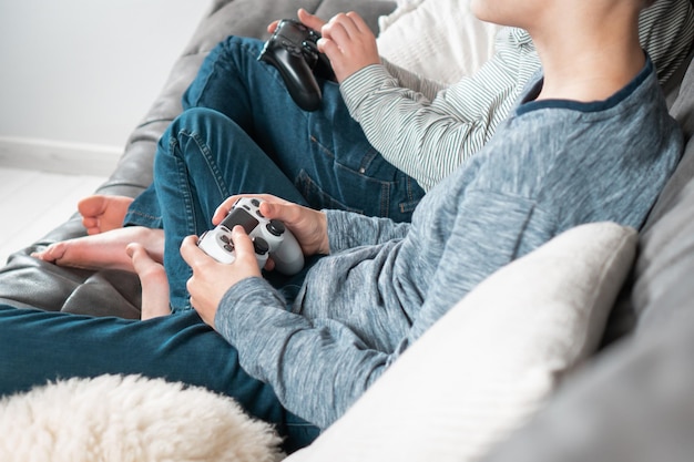 게임 조이스틱 측면 보기와 함께 소파에 앉아 있는 남자의 손 아이들은 비디오 게임을 하고 집에서 휴식을 취합니다