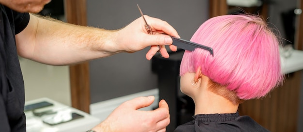 Hands of hairdresser combing hair making short pink hairstyle for a young caucasian woman in a beauty salon.