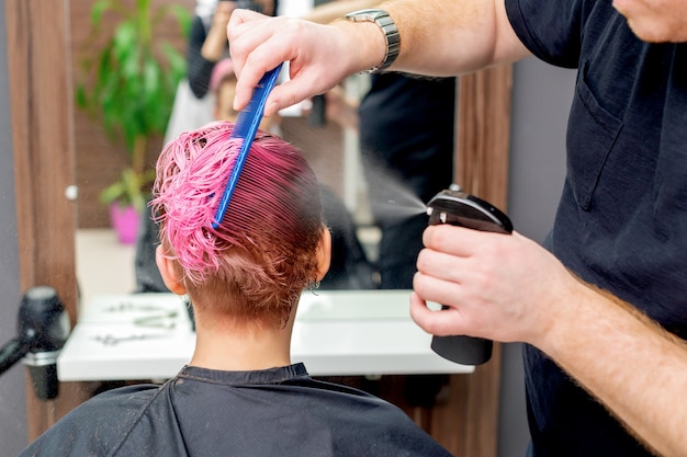 Mani del parrucchiere che spruzzano acqua sui capelli del cliente.