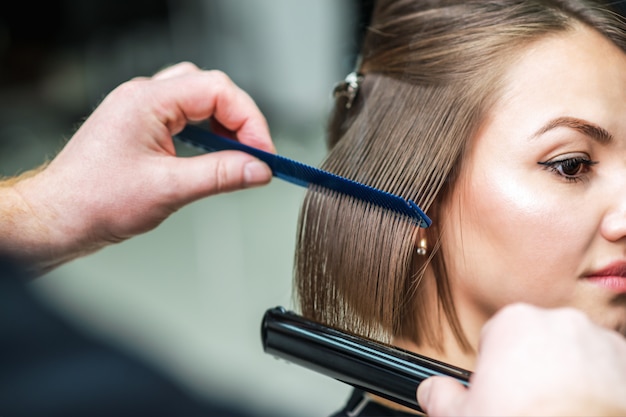 Hands of hairdresser straightening brown hair.