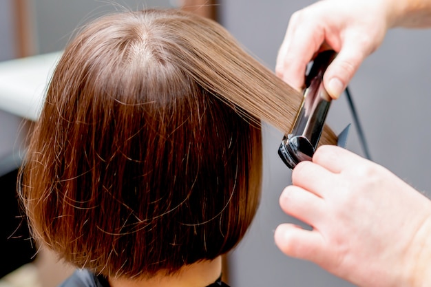 Mani del parrucchiere che raddrizzano capelli della donna.