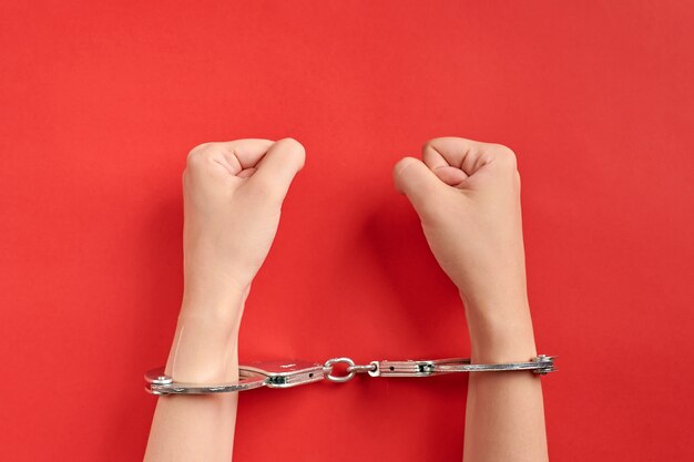 Hands in handcuffs on red background. Imprisonment concept. Deprivation of liberty and apprehend perpetrators. Fists.