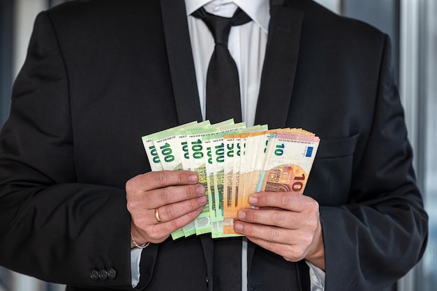 Hands of handsome businessman man in suit with euro banknotes in hands on business office background Income growth profit concept