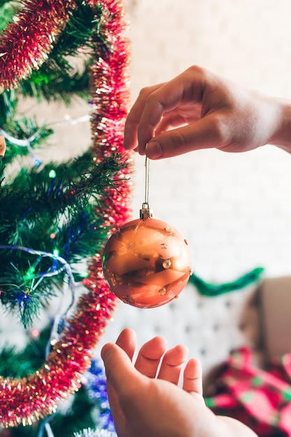 Mani appese palla dorata decorativa su pino albero di natale che decora a casa concetto invernale di famiglia di bellezza