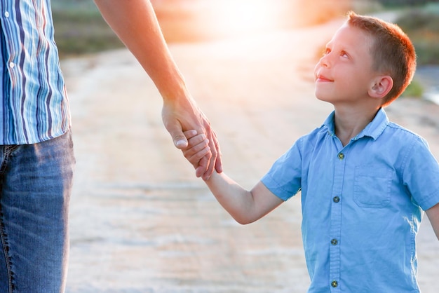 Le mani di un bambino felice e di un genitore nella natura in un parco lungo la strada