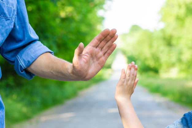 Le mani di un genitore e di un bambino felici sulla natura sulla strada sullo sfondo del parco