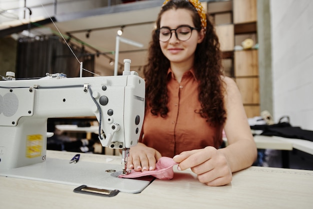 Hands of happy young seamstress by electric sewing machine making shoulder pads for new dress