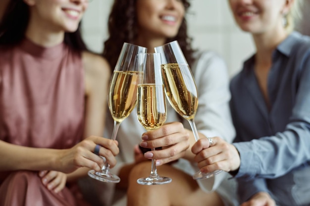 Mani di giovani donne felici che tintinnano con flauti di champagne