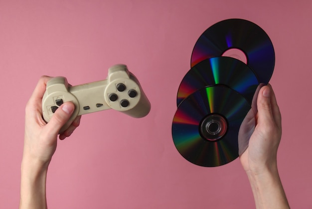 Foto le mani tengono i dischi cd e il gamepad sulla superficie pastello rosa