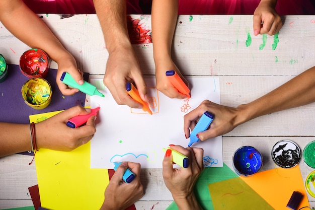 Hands hold colorful markers and draw top view