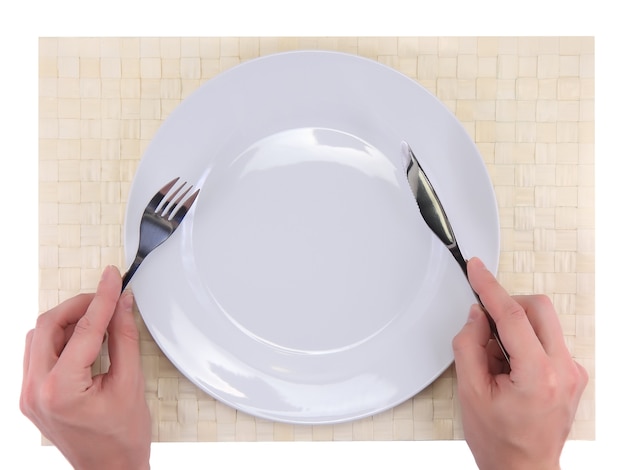 손은 대나무 매트에 있는 접시 위에 포크와 나이프를 들고 있습니다. 모든 주위에 격리.