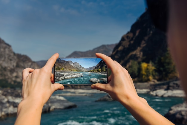 Hands hold a smartphone and take photo of mountain river and a rocks