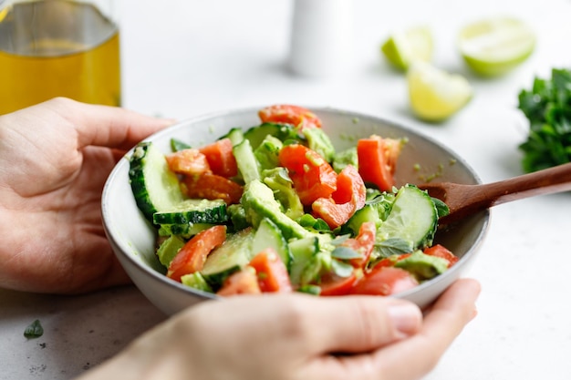 Hands hold vegetarische salade is gemaakt van avocado, tomaten, komkommer, basilicum en limoensap
