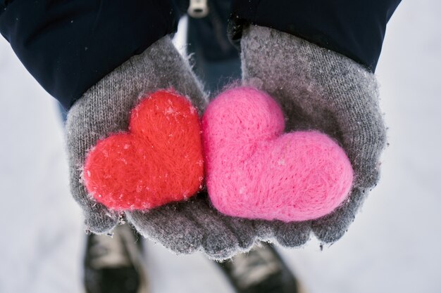 Hands hold woolen hearts covered with snowflakes outdoors in winter