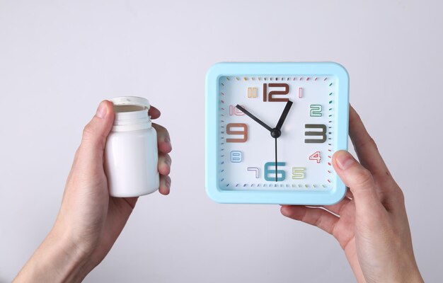 Hands holding alarm clock and pills bottle on white background