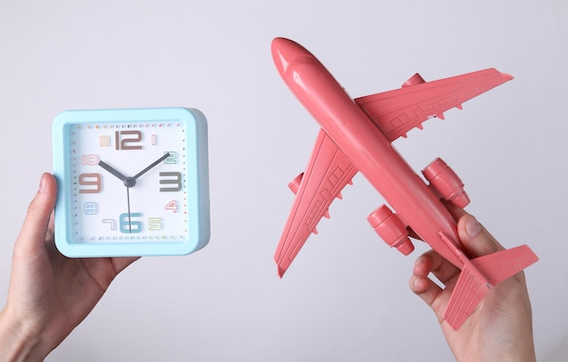 Hands holding alarm clock and plane on white background Travel time