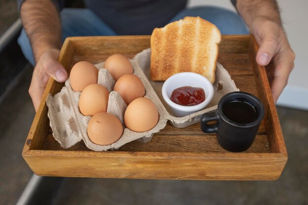 Hands holding american breakfast tray, traditional ingredients, eggs, jam and coffee
