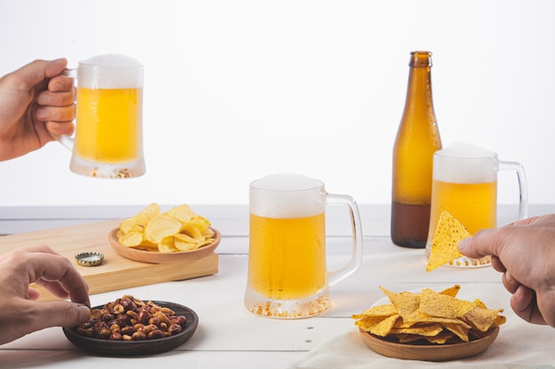 Mani che tengono birra e che dividono uno spuntino sulla base di legno bianca