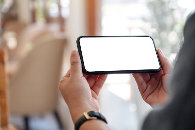 Photo hands holding black mobile phone with blank desktop screen horizontally in cafe