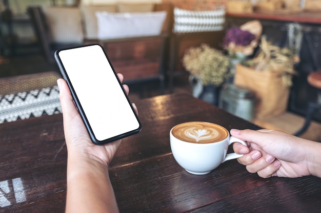  hands holding black mobile phone with blank screen while drinking coffee in vintage cafe