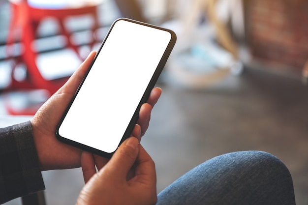 hands holding black mobile phone with blank white desktop screen in cafe