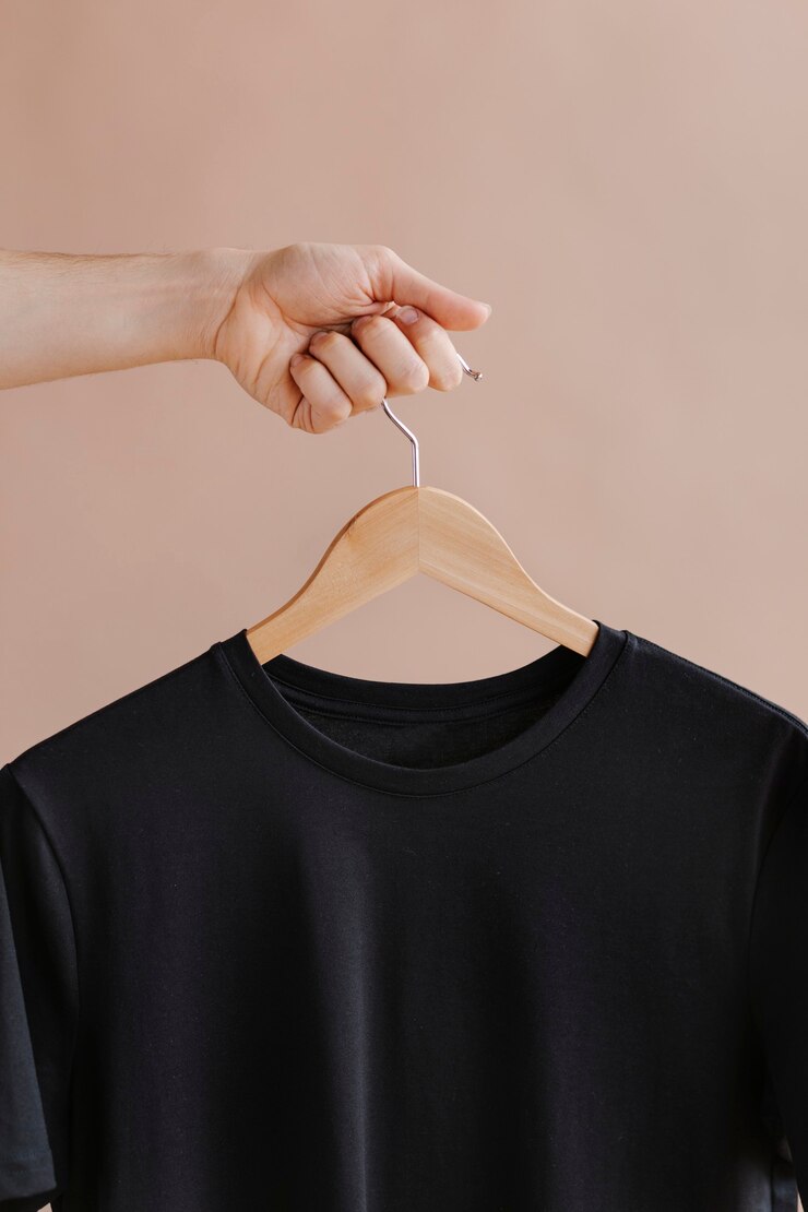 Photo hands holding a black t-shirt in a hanger