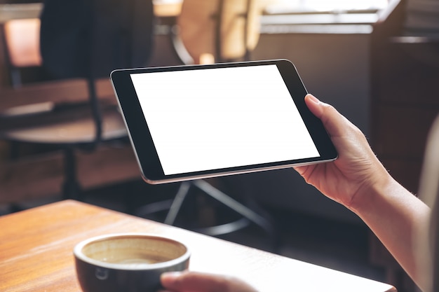 hands holding black tablet pc with blank white screen while drinking coffee