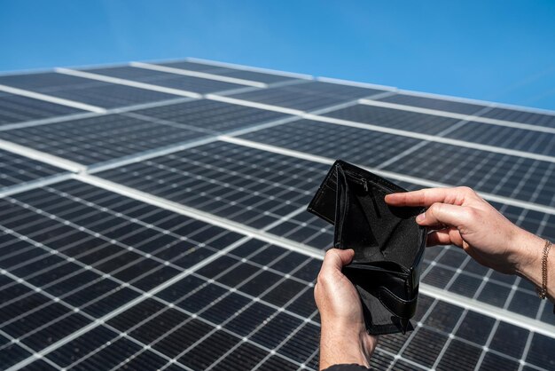 Фото Руки держат пустой черный бумажник без долларов над солнечными панелями