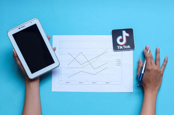 Photo hands holding blank screen tablet and pen with graph paper and tiktok logo icon. tiktok's growth tre