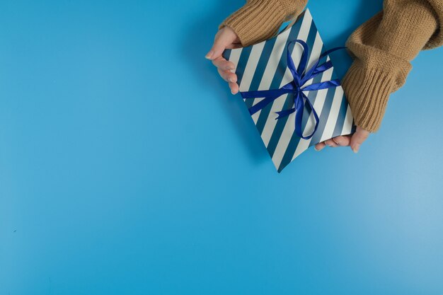 hands holding a blue and white striped gift box tied with ribbon on blue background