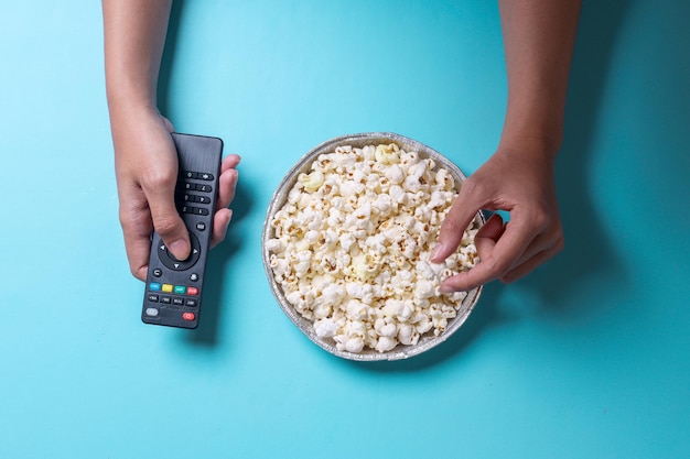 Hands holding a bowl of popcorn and remote control Entertainment concept on blue background