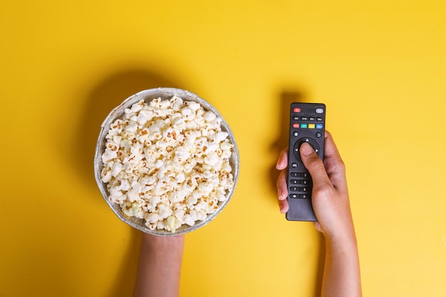 Hands holding a bowl of popcorn and remote control entertainment concept on yellow background