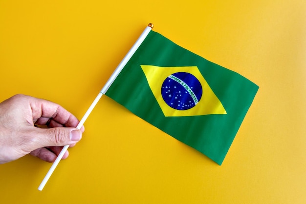 Hands holding the Brazilian flag on a yellow background