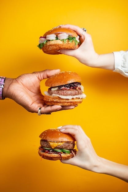 Hands holding burger against yellow background. fast food, junk\
food concept.