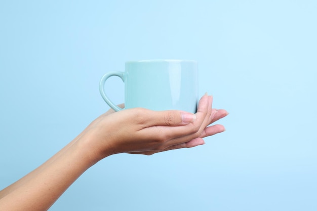 Руки, держащие керамическую чашку для макета, изолированные на синем фоне