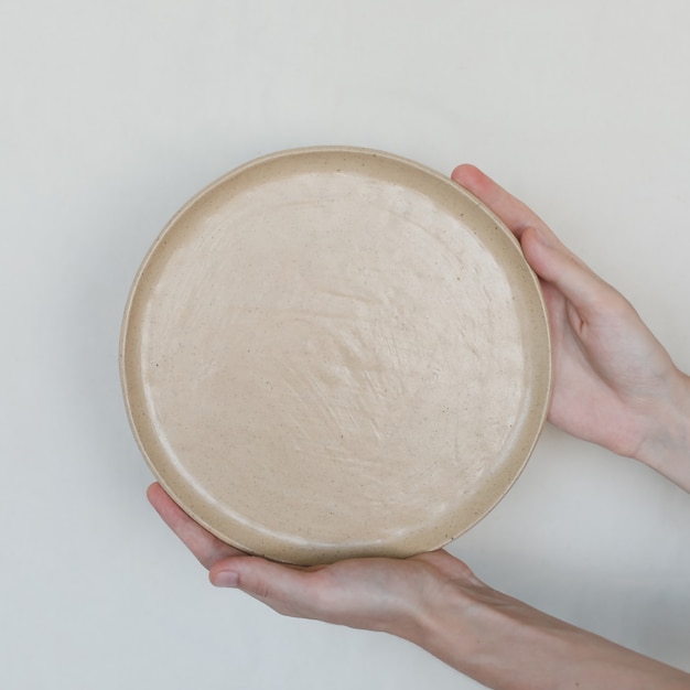 Руки, держащие керамические пластины, изолированные на белом фоне. Минималистичный набор керамической посуды и керамики ручной работы