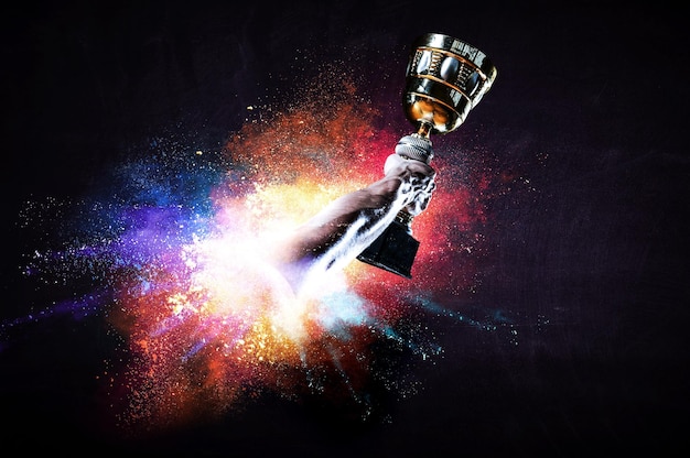 Photo hands holding champion cup on colourful splashes background. mixed media