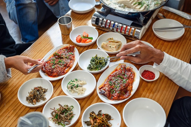 Hands holding chopsticks clamping to korean food on wooden table