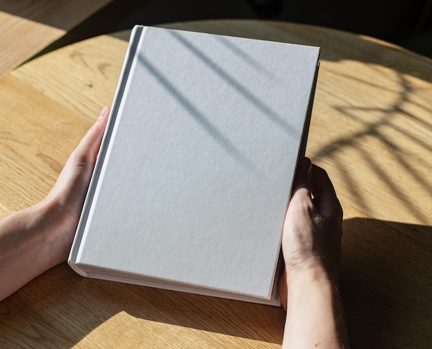 Руки держат закрытый макет книги на деревянном столе
