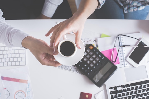 Hands holding coffee cup above desktop