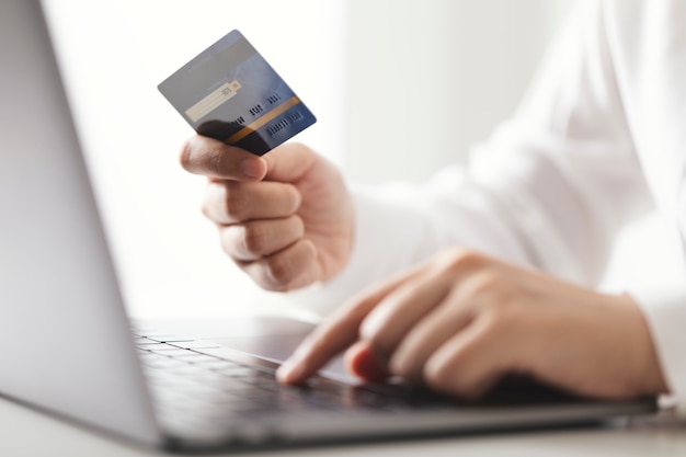 クレジットカードを持ち、ラップトップコンピューターを使用している手、在宅勤務の実業家、オンラインショッピング、eコマース、支出、インターネットバンキング。