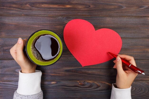 Hands holding a cup of coffee and writing valentine. 