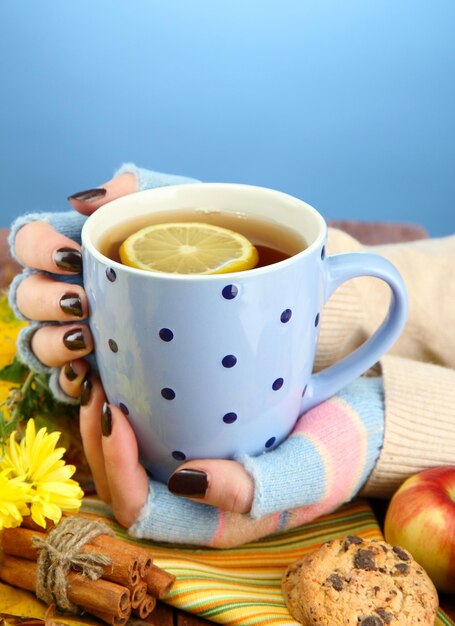 写真 青の背景に温かい飲み物と紅葉のカップを持つ手