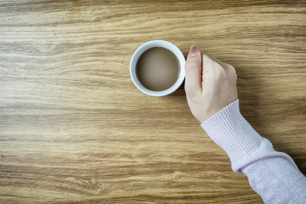 木製のテーブルの背景に熱いコーヒーのカップを持つ手のビンテージ