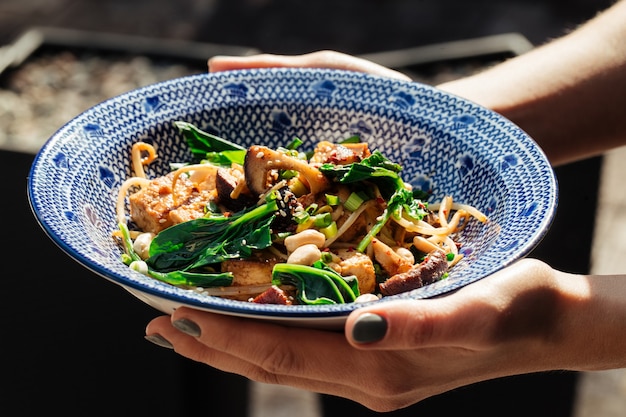 Hands holding dish of fried tofu with spinach and nuts