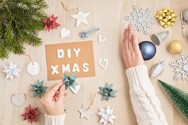 DIY、ゼロウェイスト、木製のテーブルに環境に優しいクリスマスオーナメントを持っている手、フラットレイ、上面図。代替の持続可能な、プラスチック製のクリスマスデコレーションなし