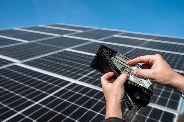 Hands holding dollar bills and wallet over solar panels